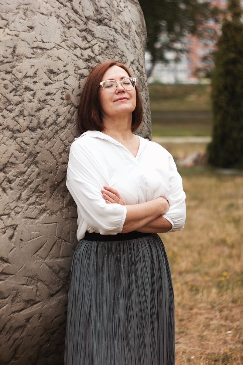woman in white long sleeve shirt and dark gray skirt standing beside brown clay rock during daytime